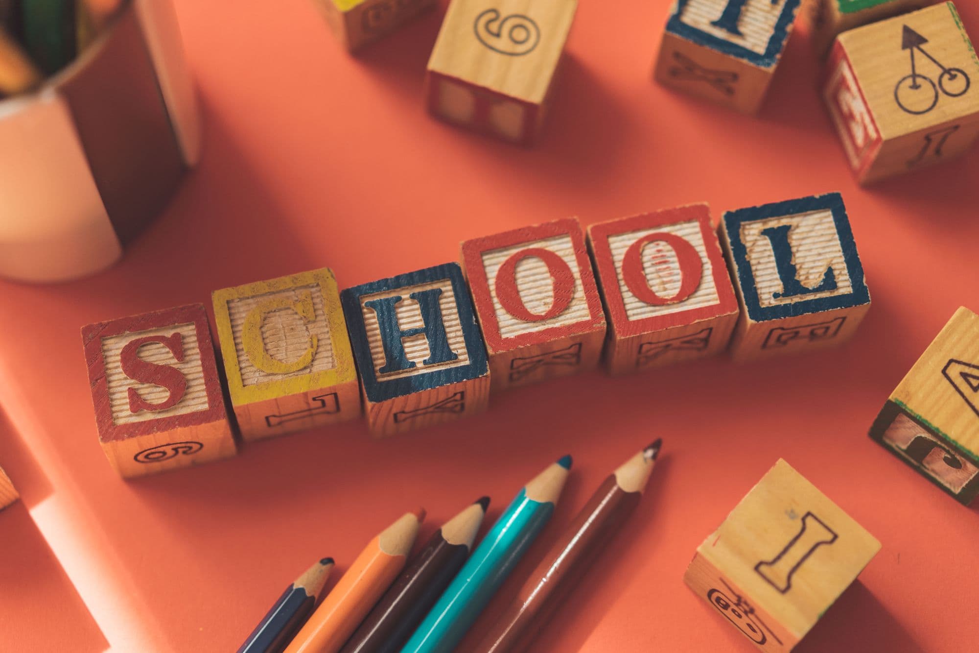 Houten blokjes die samen het woord 'school' vormen, naast kleurpotloden
